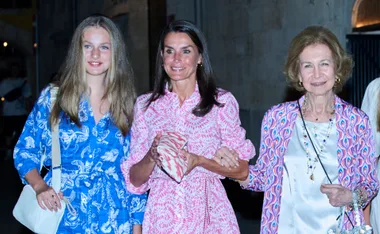 Three women in colorful dresses smiling at an evening event, one in pink and two in blue patterns.
