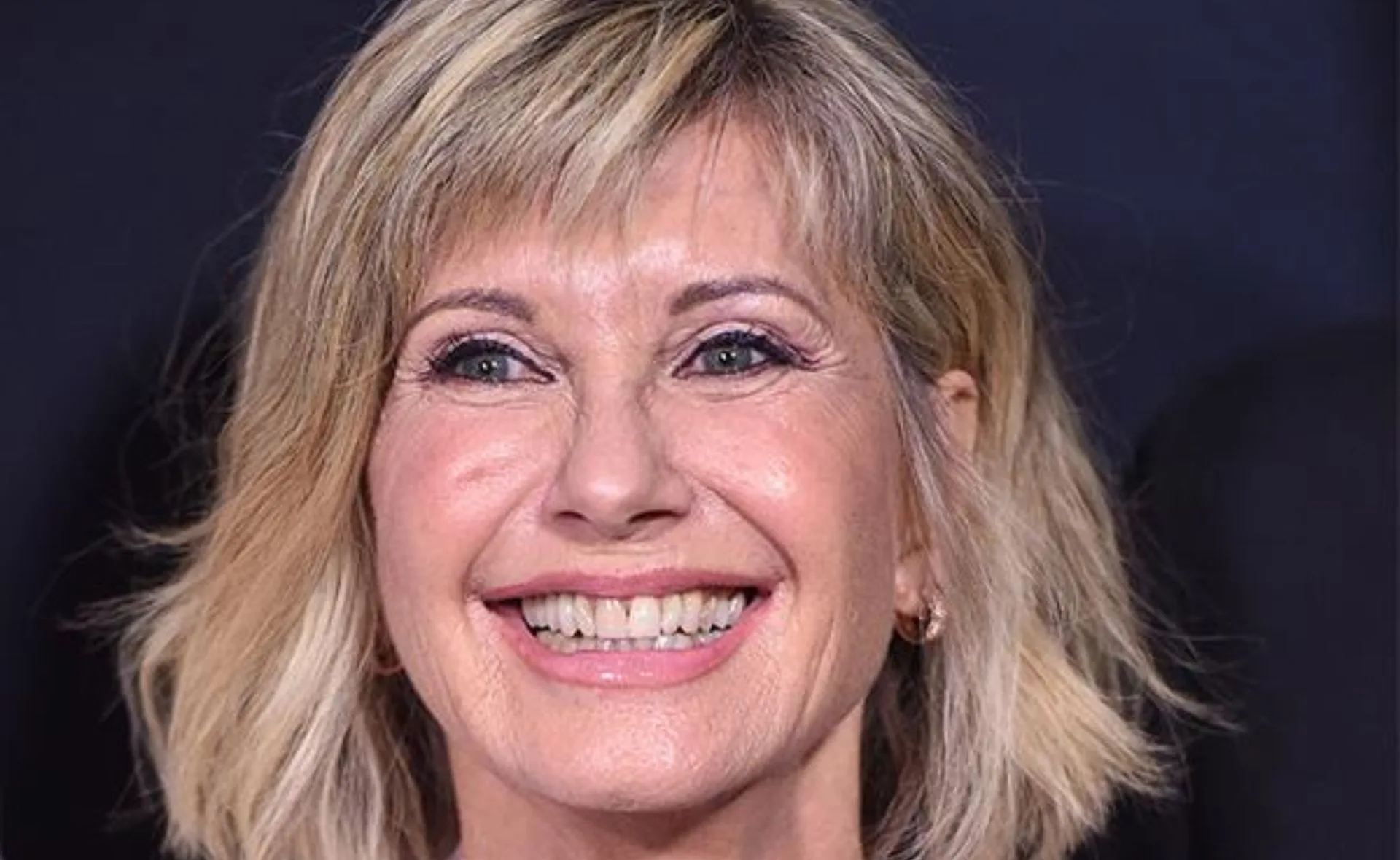 Smiling woman with short blonde hair on a dark background.