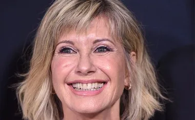 Smiling woman with short blonde hair on a dark background.
