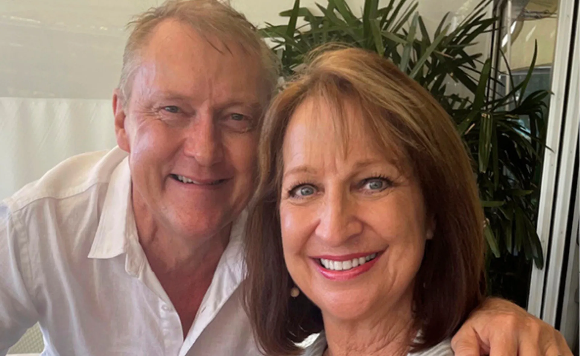 A man and woman smiling together with green plants in the background.