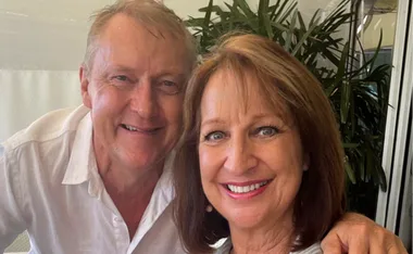 A man and woman smiling together with green plants in the background.