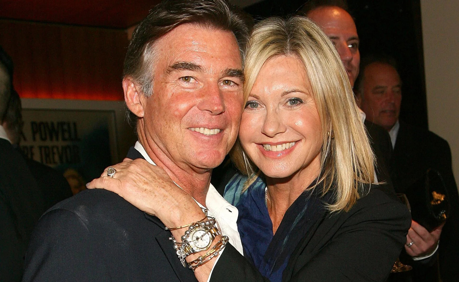 Couple smiling and embracing at an event, with the woman wearing a watch and bracelets.