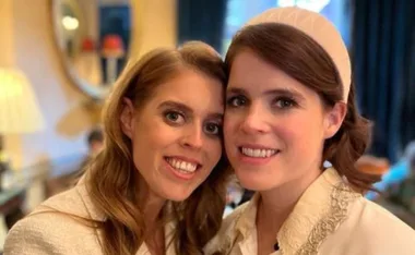 Two women smiling together in a warmly lit room, with elegant decor and a mirror in the background.