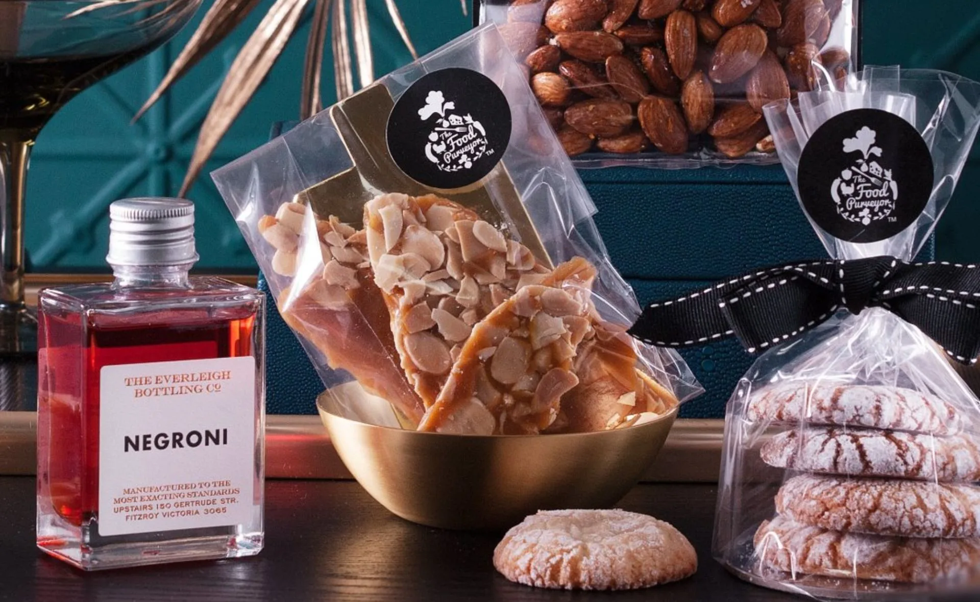 Gift hamper with Negroni bottle, almond snacks, cookies, and nuts in elegant packaging.