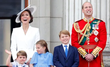 A family on a balcony smiles and waves, dressed in formal attire, with a woman in a white hat and a man in a red military uniform.