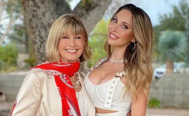 Two smiling women posing together outdoors, one wearing a red scarf, the other in a white dress.