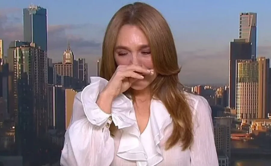 Woman in white blouse with hand on face, emotional in front of city skyline.