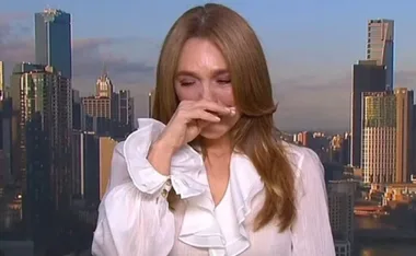 Woman in white blouse with hand on face, emotional in front of city skyline.