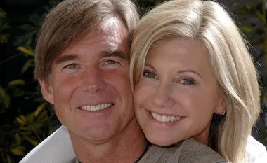 Olivia Newton-John and John Easterling smiling together, outdoors in sunlight.
