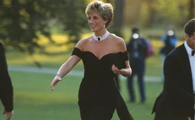 Princess Diana in an off-shoulder black dress with a choker necklace, smiling and walking outdoors.