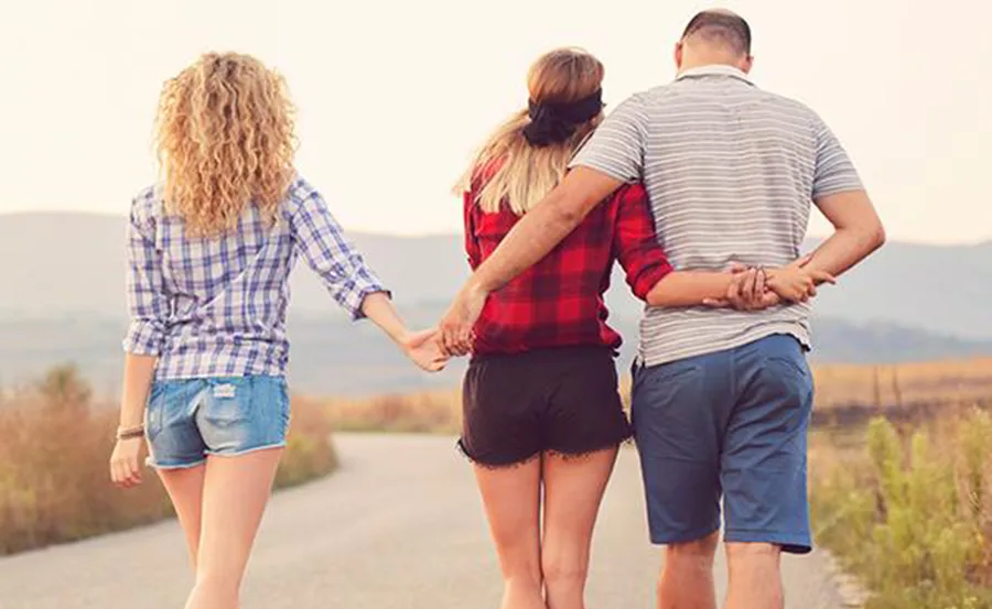 A woman walks holding hands with a man and another woman on a rural path, all facing away from the camera.