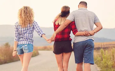 A woman walks holding hands with a man and another woman on a rural path, all facing away from the camera.