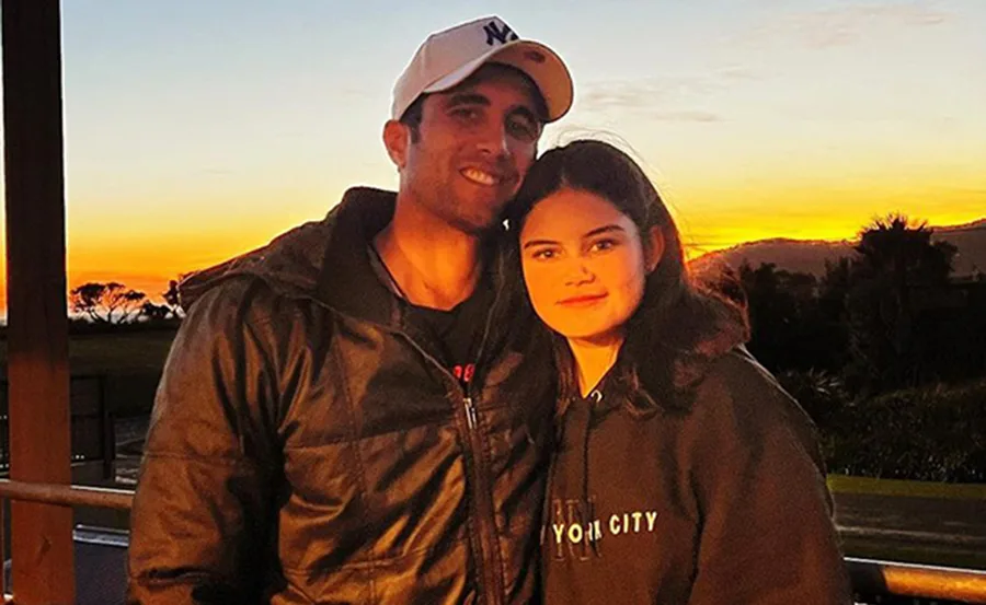 Man and young woman smiling at the camera, standing together at sunset on a terrace with scenic view.