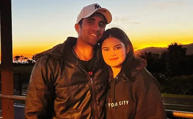 Man and young woman smiling at the camera, standing together at sunset on a terrace with scenic view.