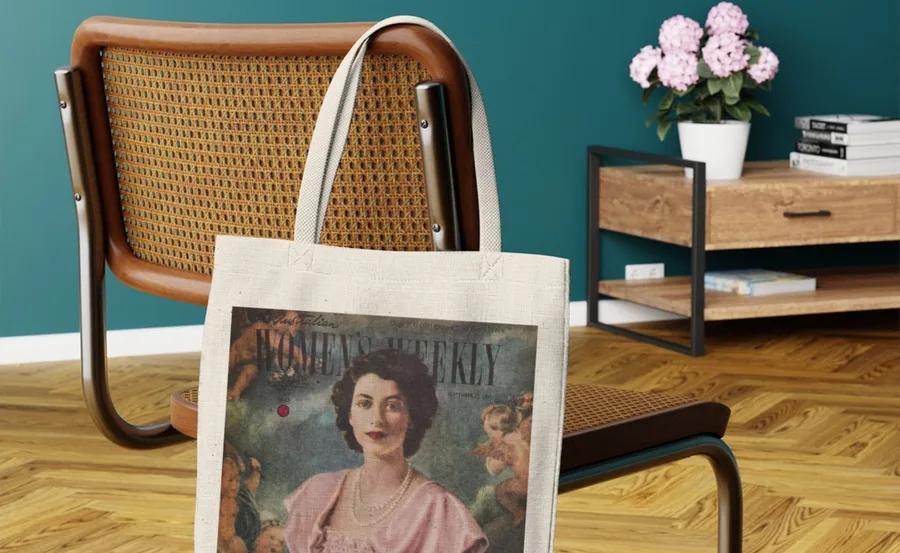 Tote bag with vintage Women's Weekly cover featuring a portrait of Queen Elizabeth II, draped over a chair.