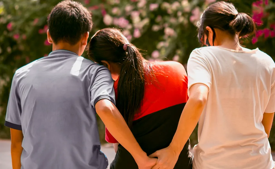 A man with his arm around a woman, holding hands secretly with another woman behind her back.