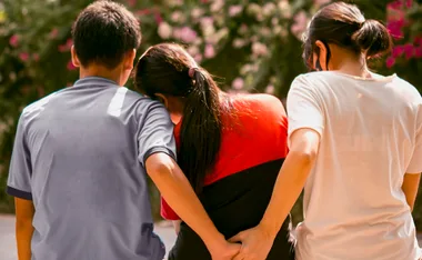 A man with his arm around a woman, holding hands secretly with another woman behind her back.