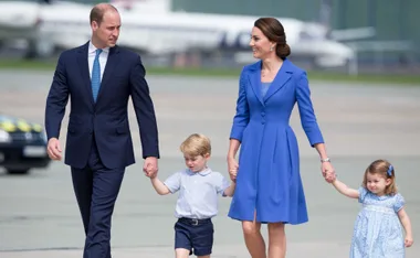 A family of four walking on an airport tarmac, parents holding hands with two children.