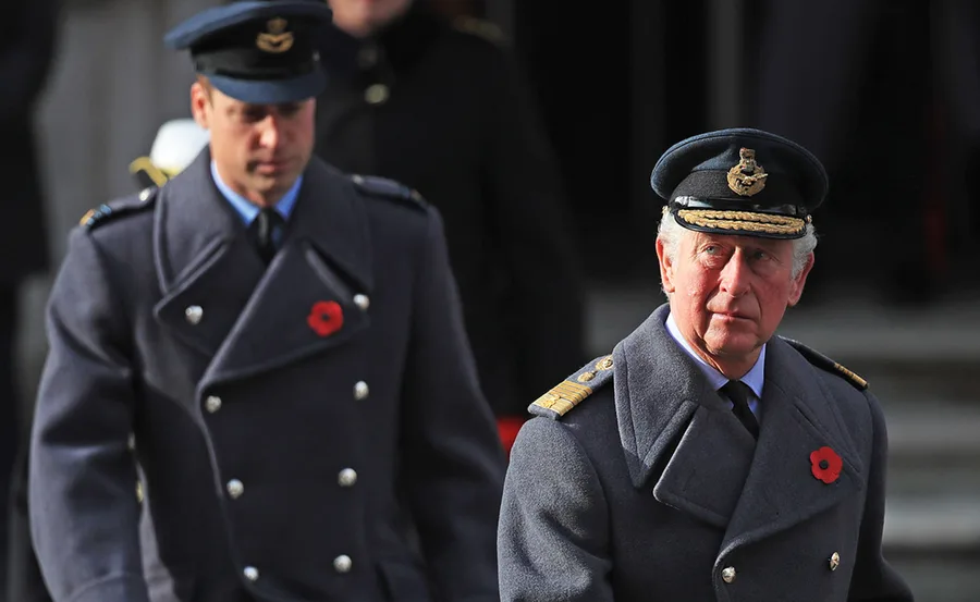 Two men in military uniforms with poppies on their coats, standing outdoors.
