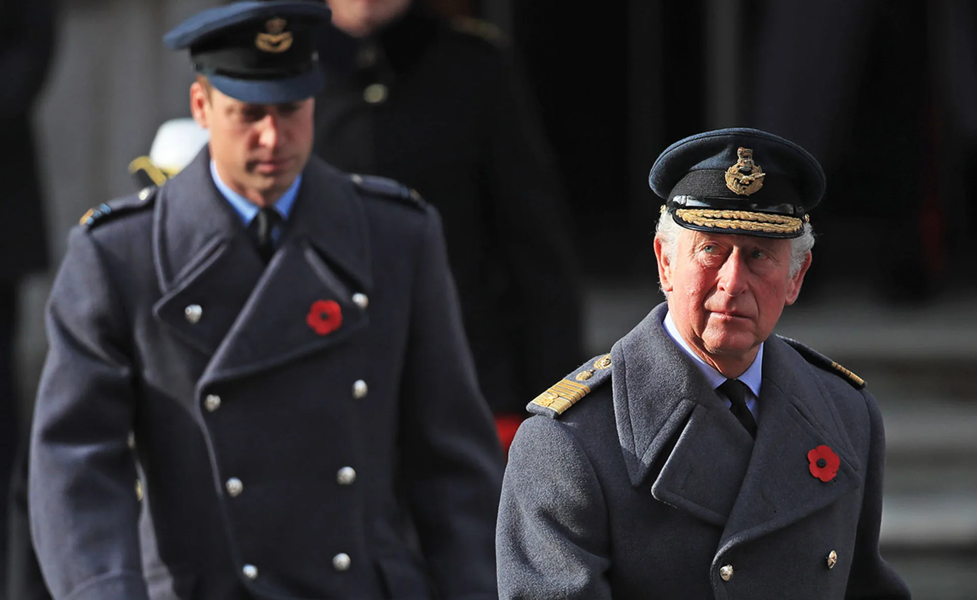 Two men in military uniforms with poppies on their coats, standing outdoors.