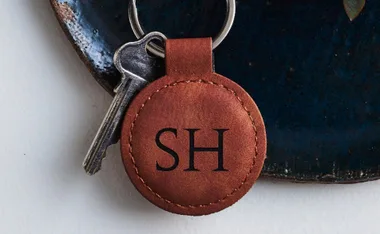Keychain with brown leather tag engraved "SH" next to a silver key on a dark ceramic surface.