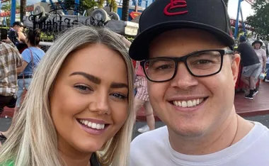 A couple smiling together at a theme park with a ride in the background.