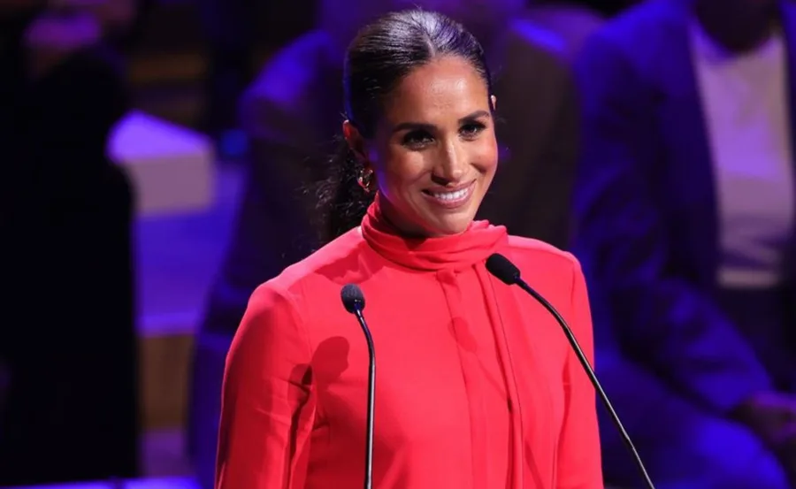 Woman in a red outfit speaking at a podium with two microphones.