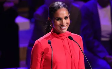 Woman in a red outfit speaking at a podium with two microphones.