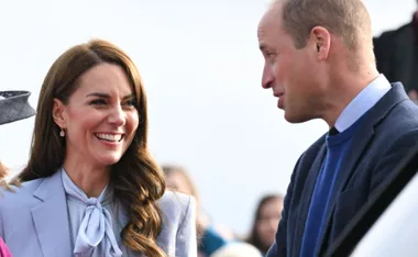 A smiling couple in conversation, outdoors, with a blurred crowd in the background.