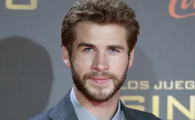 Actor in a suit with a beard and short hair at a formal event background.