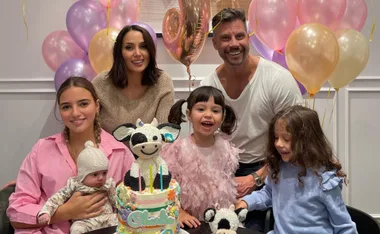 Family celebrating a birthday with colorful balloons, a cake with a cow figurine, and smiling children.