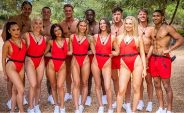 A group of Love Island Australia contestants standing outdoors in red swimwear and smiling at the camera.