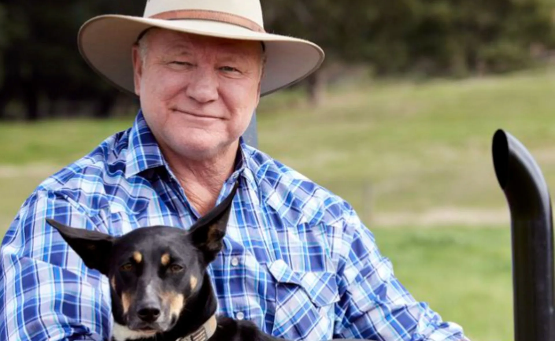 Elderly man in a hat holding a black and tan dog on his lap outdoors, both looking at the camera.