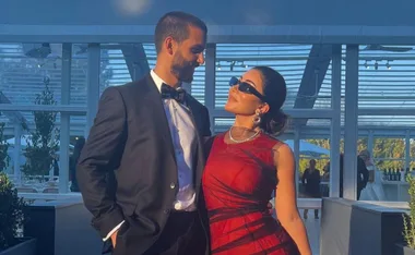 Elegant couple gazing at each other, with the woman in a red dress and sunglasses.