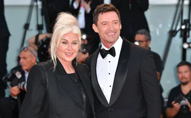 "Two people in formal attire smiling at a red carpet event."