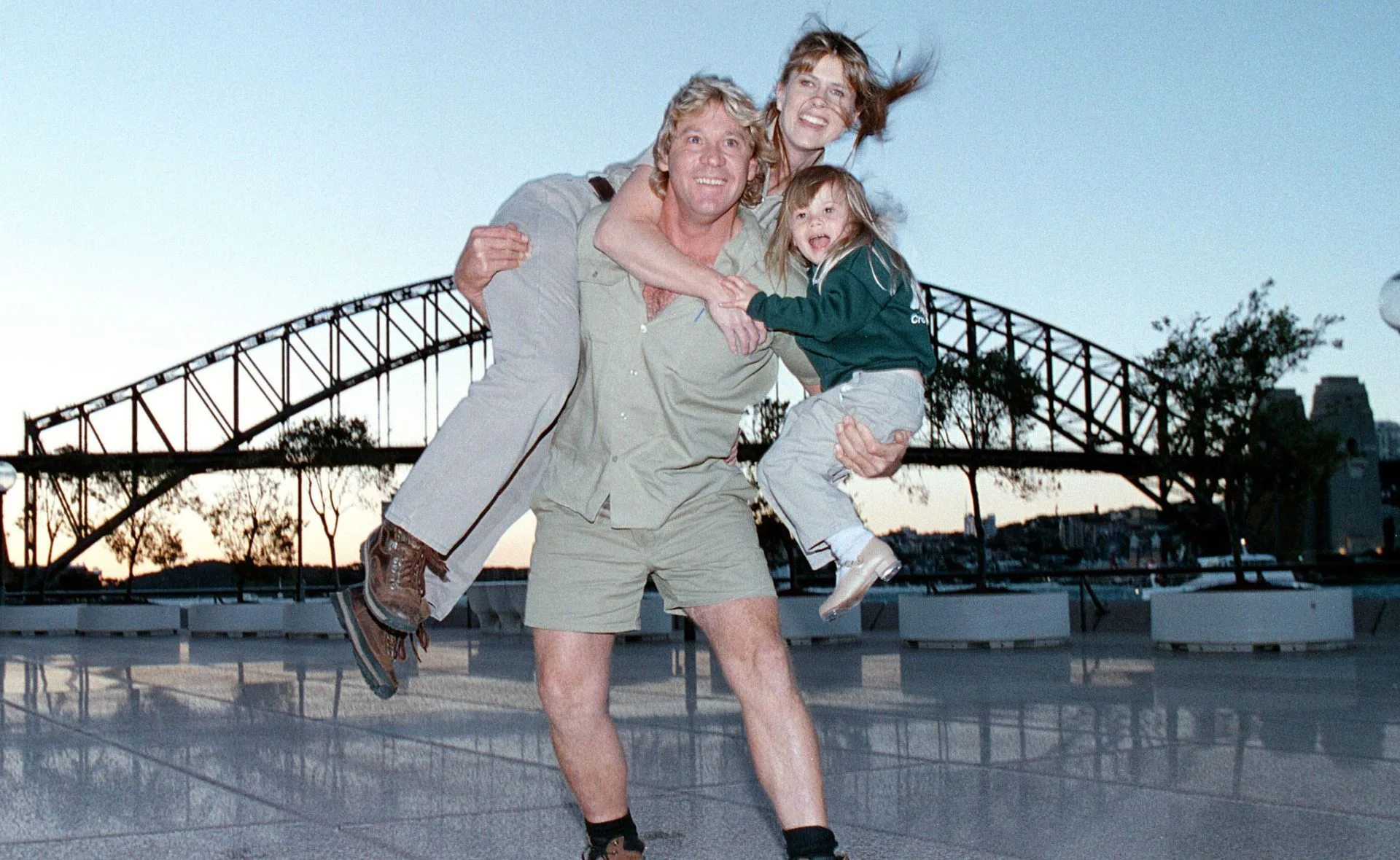 A family poses playfully with a scenic bridge as the backdrop during sunset.