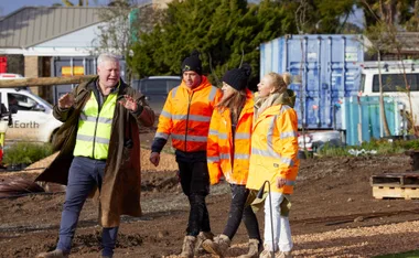 Four people in fluorescent jackets walk through a construction site, engaged in conversation.