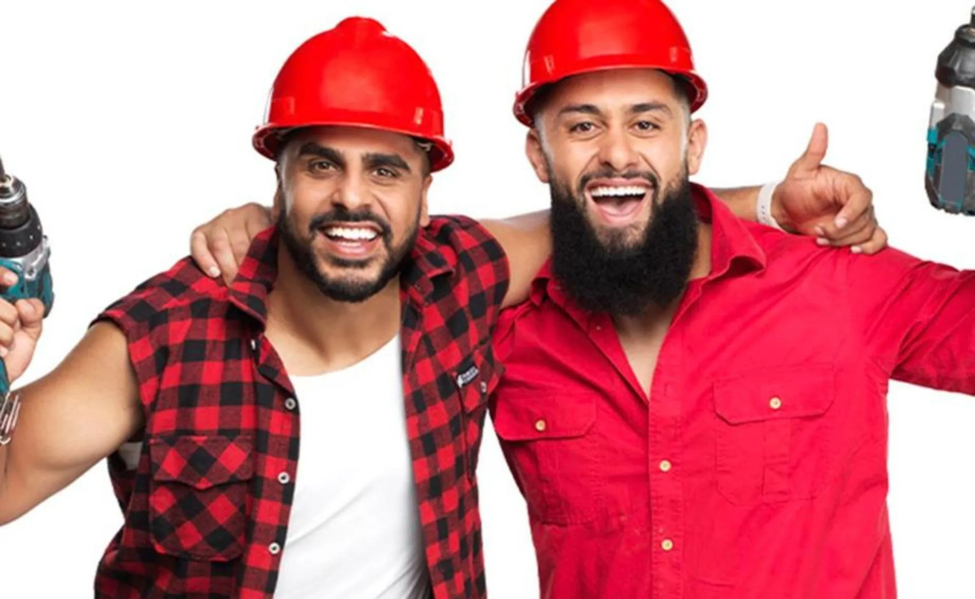 Two men wearing red construction helmets, smiling and holding power tools, with arms around each other in a friendly pose.