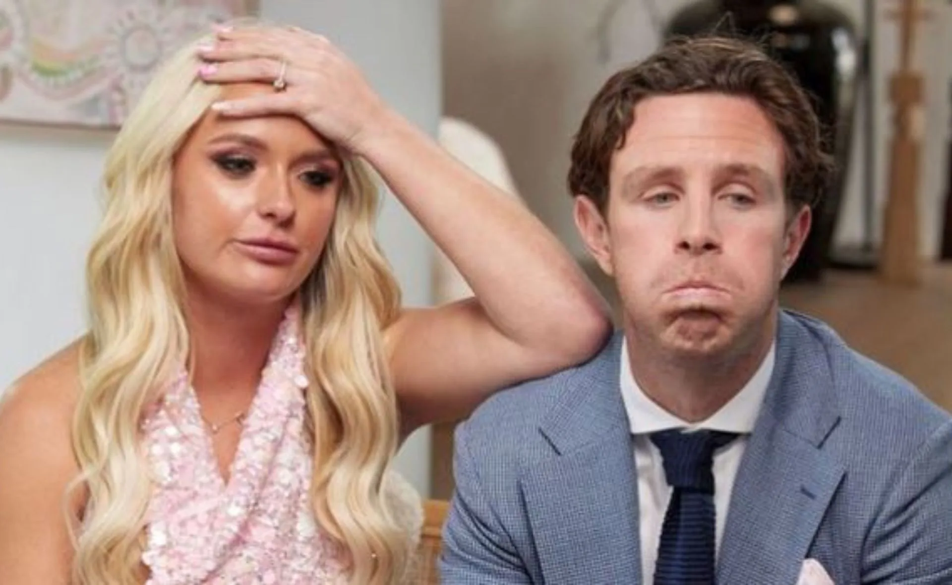 A worried-looking woman with long blonde hair sits beside a man in a blue suit, both expressing concern.