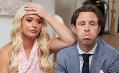 A worried-looking woman with long blonde hair sits beside a man in a blue suit, both expressing concern.