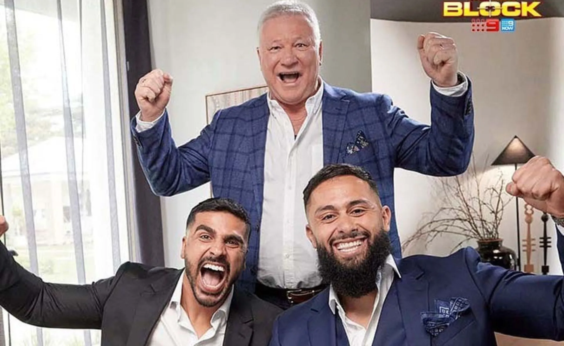 Three men in suits celebrating, smiling and raising fists in a room with "The Block" logo in the corner.