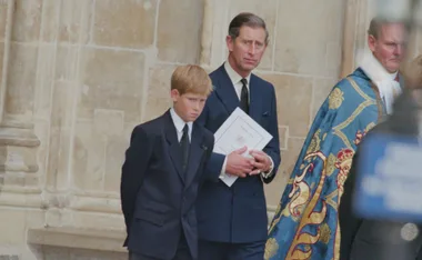 A young boy and a man in formal attire at a solemn event, holding a document, with a clergy member nearby.