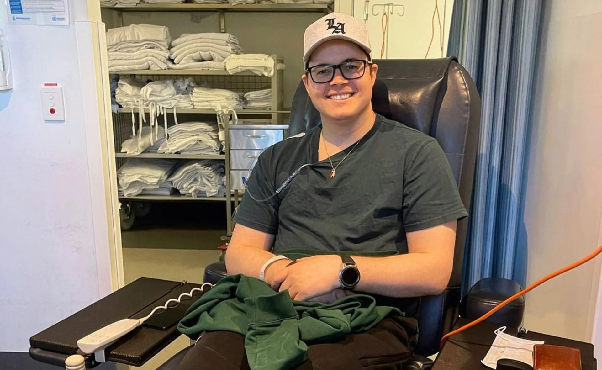 Man sitting in a chair, wearing a cap, receiving treatment with medical equipment in a clinic room.