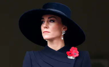 A person wearing a wide-brimmed black hat and pearl earrings, with red poppy flowers on the outfit.