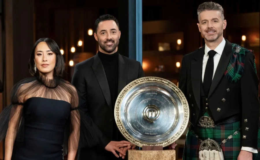 Three judges standing with the MasterChef Australia trophy; one wears a black dress, another a suit, and the third a kilt.