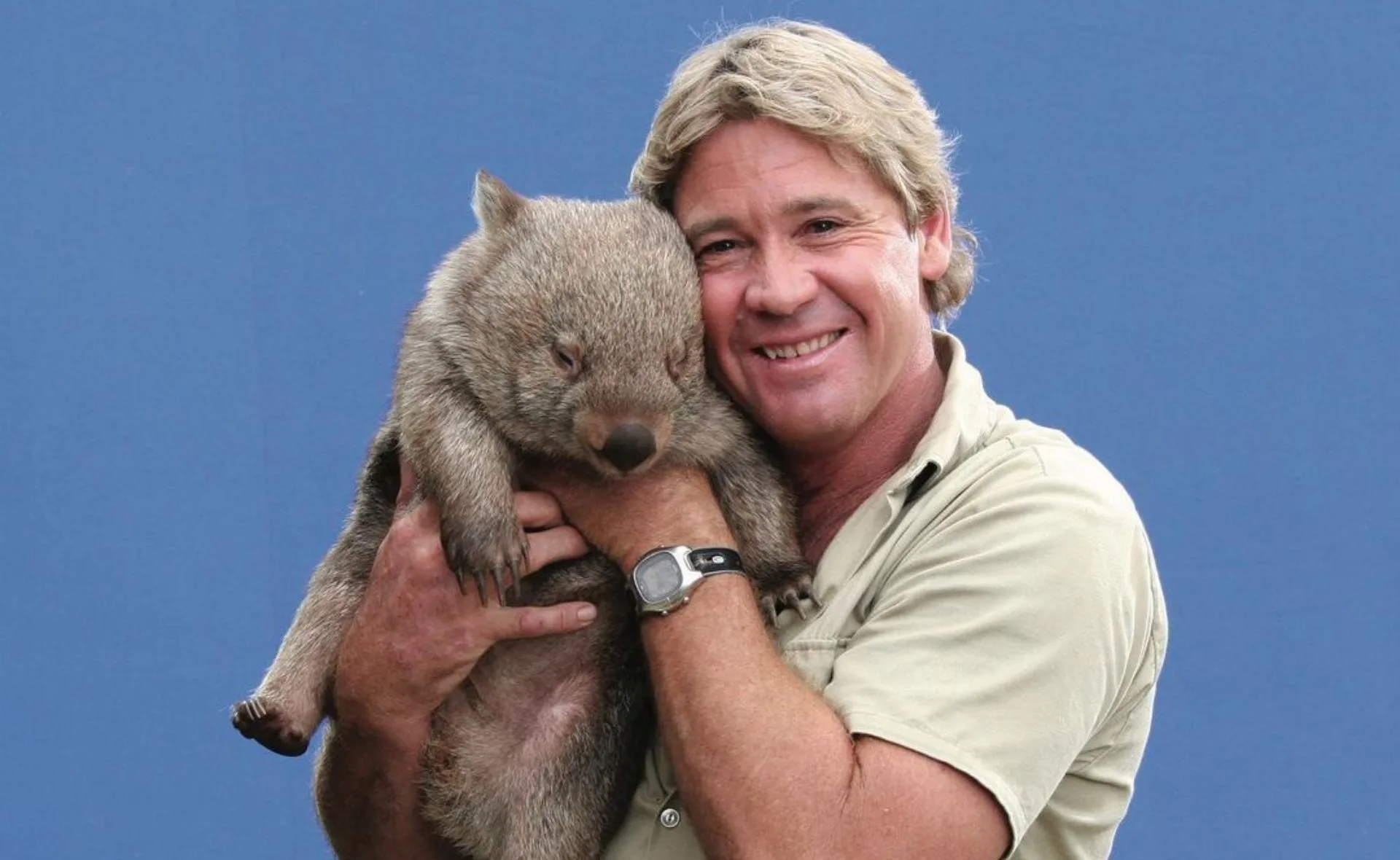Man smiling while holding a wombat against a blue background.