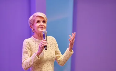 Former politician speaking at a leadership event, holding a microphone on a stage.
