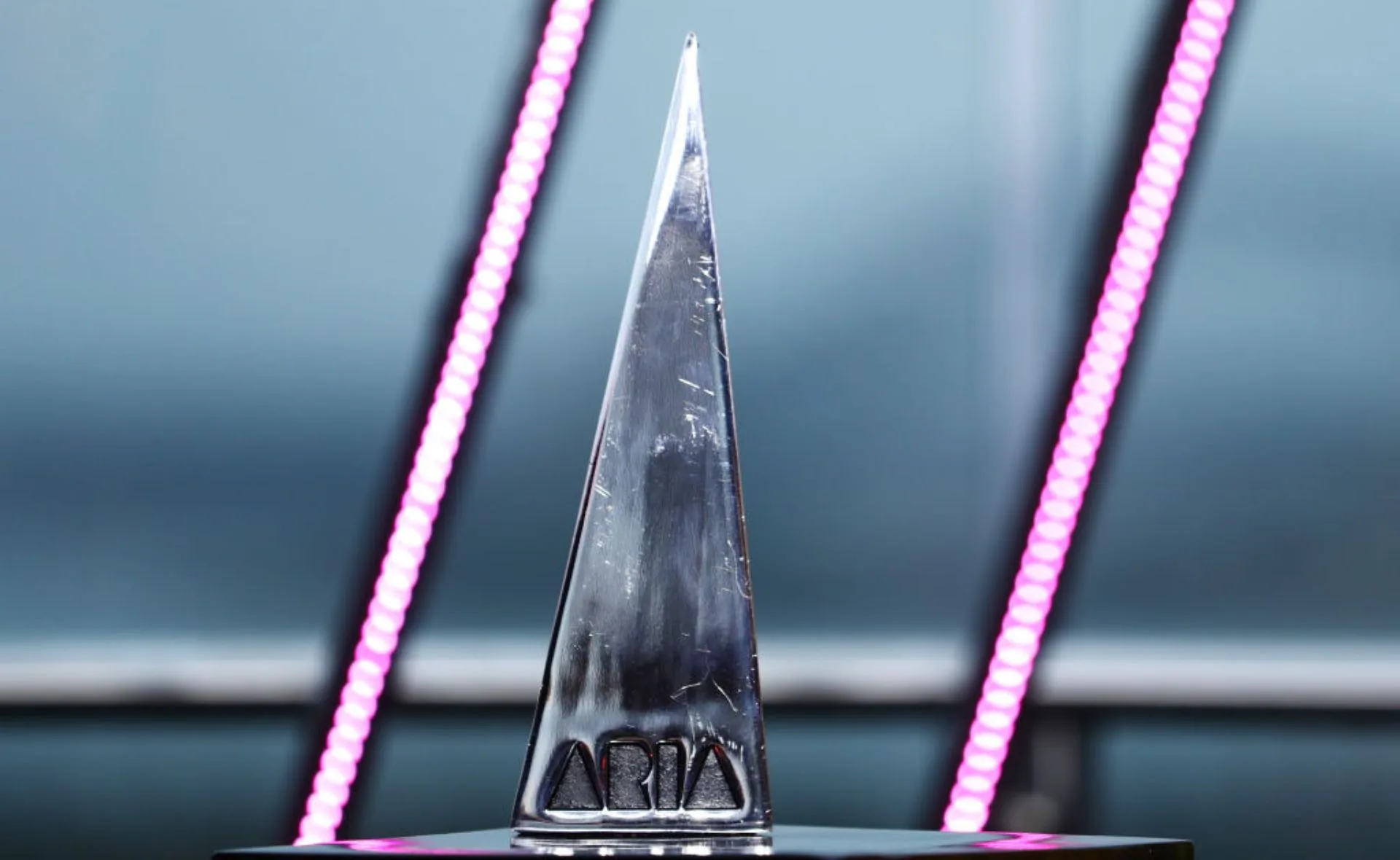 ARIA Award trophy on display, silver with a pointed top, set against a background with pink lights.