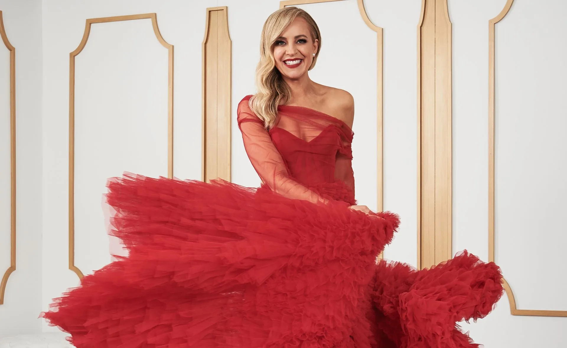 Person in a vibrant red gown standing in a stylish room with wooden panels.