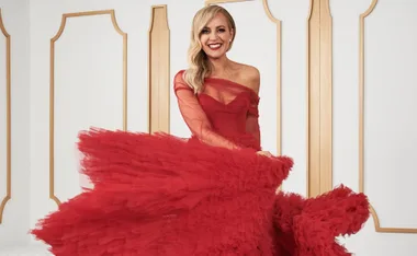 Person in a vibrant red gown standing in a stylish room with wooden panels.